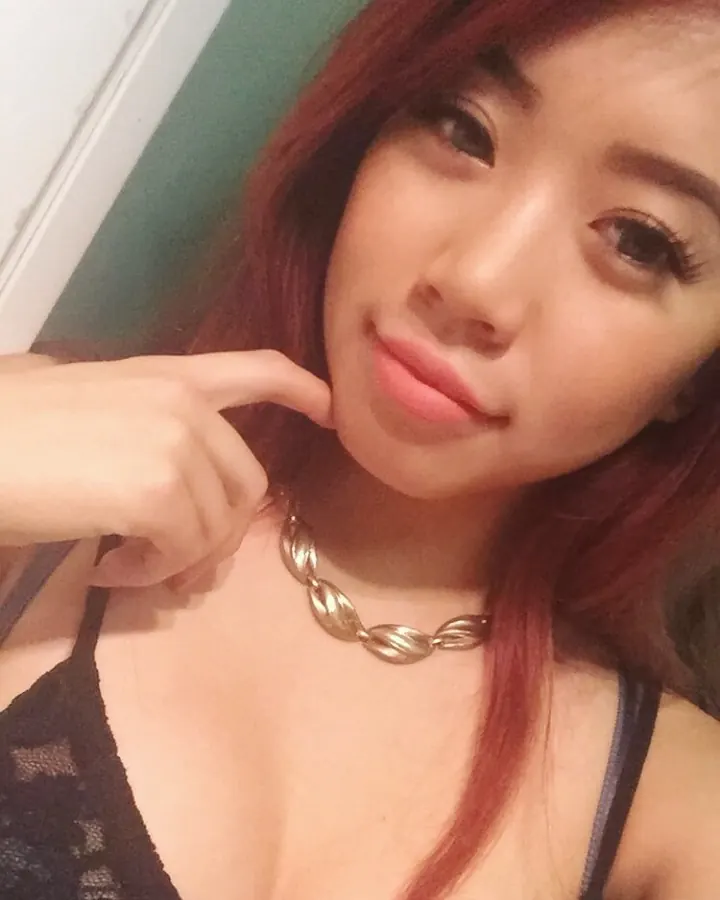 Femme trans aux cheveux roux, en sous-vêtements noirs, posant sur un lit