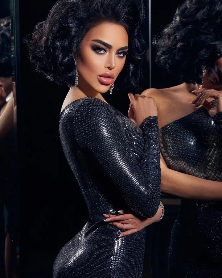 Femme trans aux cheveux bruns-noirs, en sous-vêtements noirs, posant sur un lit