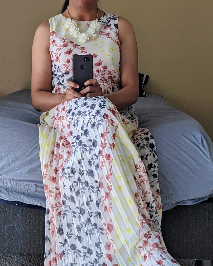 Femme trans aux cheveux noirs, portant des lunettes et une robe fleurie, assise sur un lit en tenant un téléphone