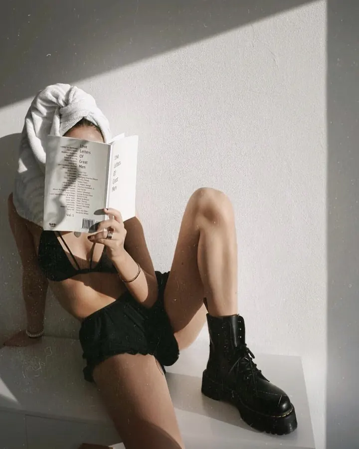 Sophie assise, livre devant le visage, short noir et bottes