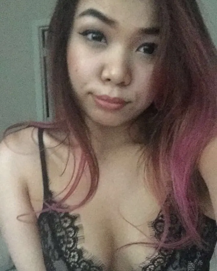 Jeune femme trans asiatique aux cheveux bruns avec reflets roses, portant un soutien-gorge noir en dentelle, regardant l'appareil photo.