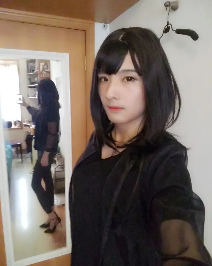 Femme trans en bikini multicolore, cheveux bruns, pose de profil, regard vers l'objectif, fond extérieur.