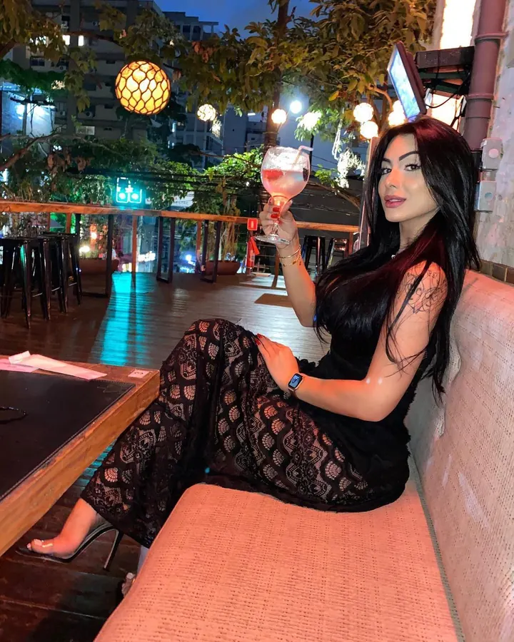 Femme en robe noire dentelle tenant un verre rose sur terrasse
