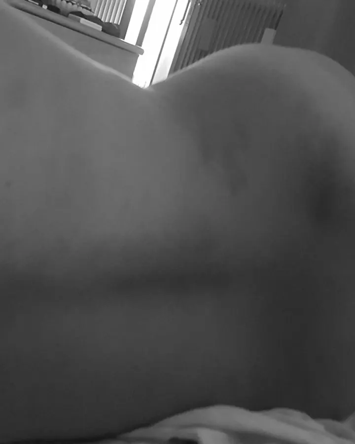 Femme trans aux cheveux noirs, en lingerie noire, posant sur un lit.