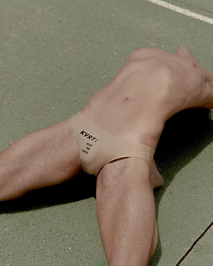Homme nu, portant un sous-vêtement beige, allongé sur un sol vert.